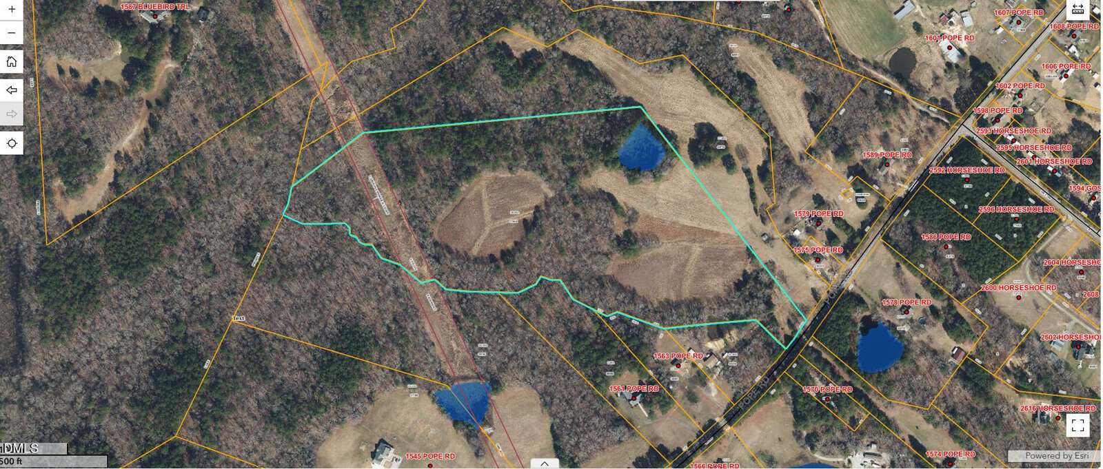 Aerial map view showing a large, irregularly-shaped property outlined in green with ponds, fields, wooded areas, and nearby roads and residential parcels labeled in red. Roads and property lines are also visible.