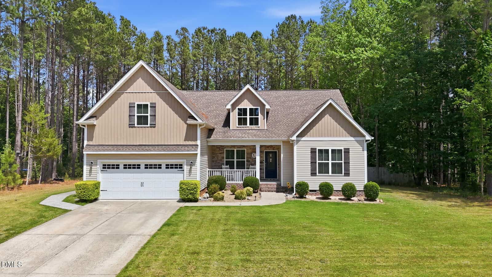 A beige, two-story suburban house at 906 Weatherby Lane in Creedmoor features a gabled roof, attached two-car garage, covered front porch, and manicured lawn, set against tall trees under a blue sky.