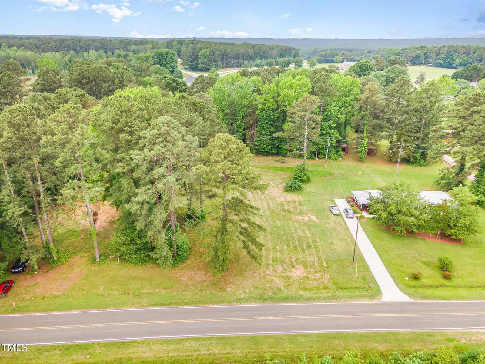 Aerial view of 71 Mount Olivet Church Road in Franklinton, featuring a rural road with a driveway leading to a house nestled among trees, open grassy areas, and a wooded forest under a partly cloudy sky.
