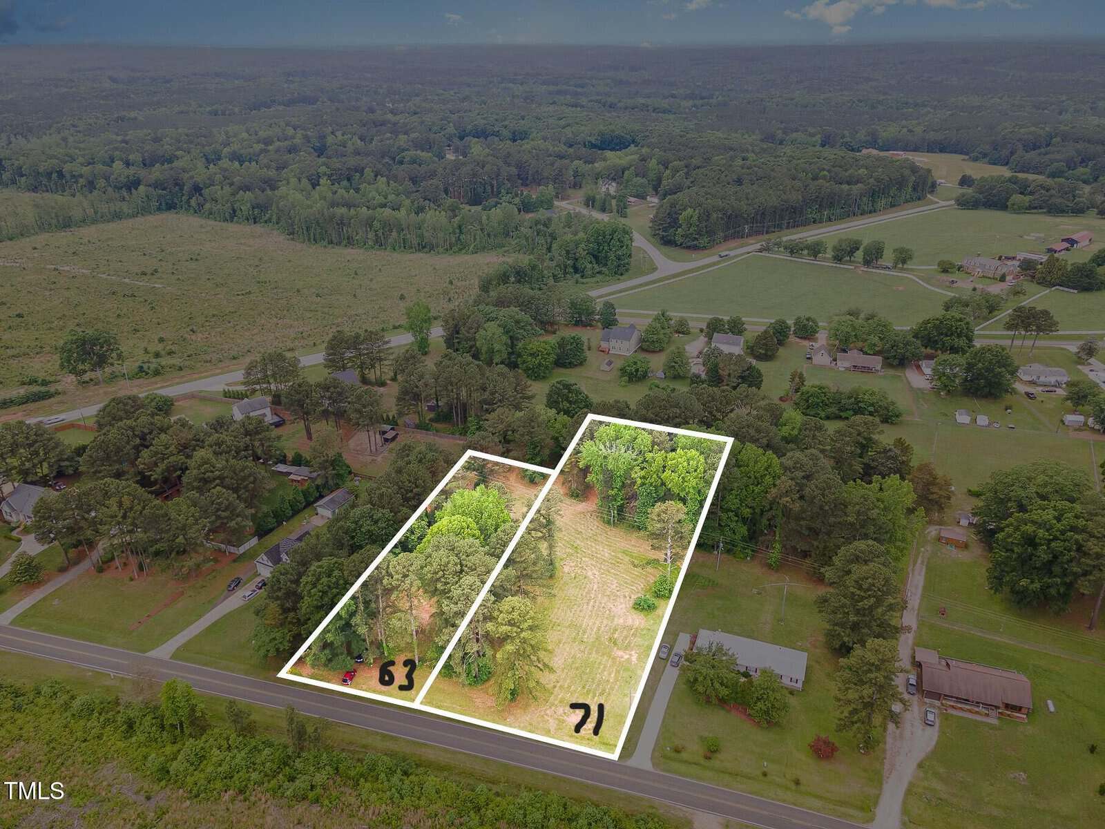 Aerial view of two adjacent rectangular plots of land outlined in white, labeled "63" and "71," surrounded by trees, roads, and scattered houses in a rural area.