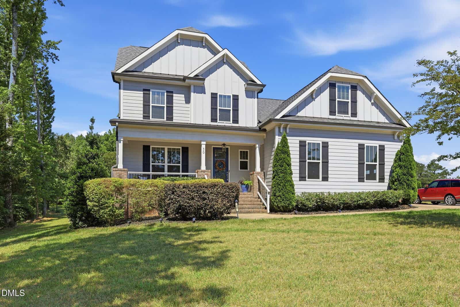 A two-story white house with gray roof shingles, large windows, and a covered front porch sits on a green lawn at 30 Willow Bend Drive, Youngsville. Trimmed bushes line the front, and a red vehicle is parked to the right under a blue sky.