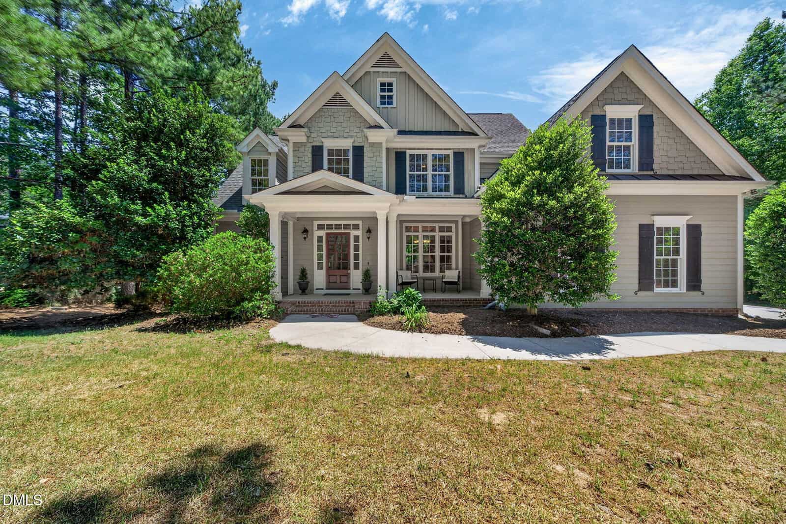 A two-story house at 150 Rivers Edge Drive in Youngsville features light gray siding, white trim, and dark shutters, surrounded by green trees and bushes with a concrete walkway leading to the front porch under a sunny, blue sky.