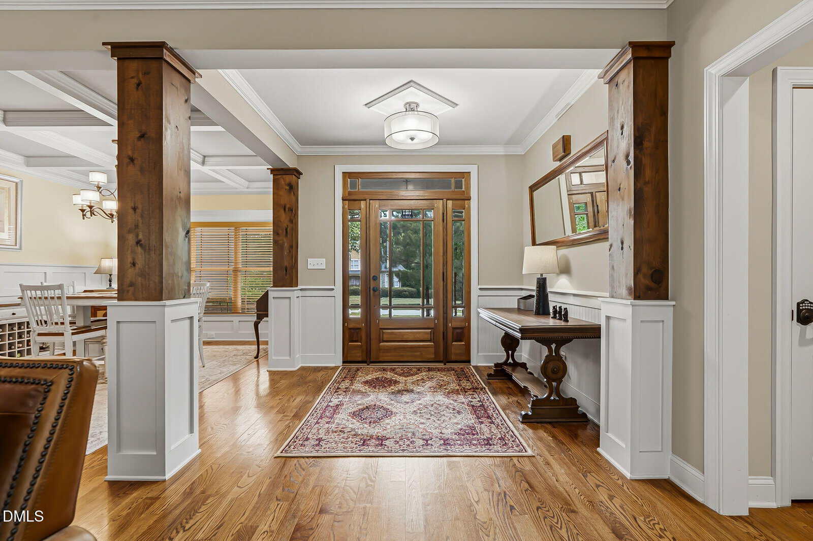 Bright, elegant entryway at 90 Pebble Creek Drive in Franklinton features wooden floors, double doors with glass panels, a patterned rug, wooden columns, console table with lamp and decor, plus an adjacent dining room with large windows.