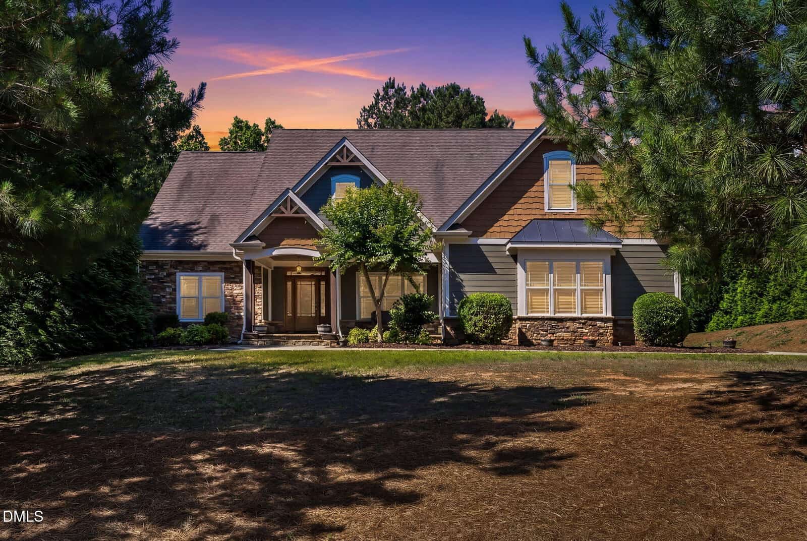 A charming single-family house with a front porch, gabled roof, and stone accents, surrounded by trees and bushes, shown at sunset with a vibrant sky in the background.