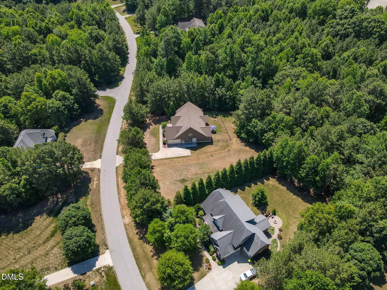 Aerial view of two large houses with driveways on spacious lots surrounded by green trees, situated along a winding road in a suburban neighborhood.