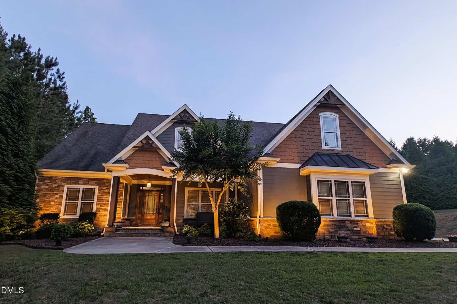 A single-story suburban house in Franklinton at 90 Pebble Creek Drive features gabled rooflines, large front windows, a covered porch, and exterior lights illuminating the entrance and landscaping at dusk. Shrubs and a small tree grace the front yard.