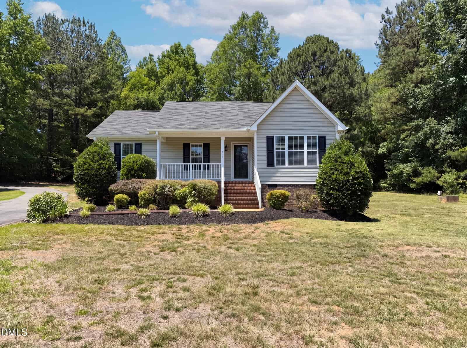 Charming single-story home at 2137 Sterling Creek Lane, Franklinton, with a front porch, white railings, and dark shutters. Surrounded by shrubs and trees, it sits on a spacious grassy lawn beneath a partly cloudy sky.