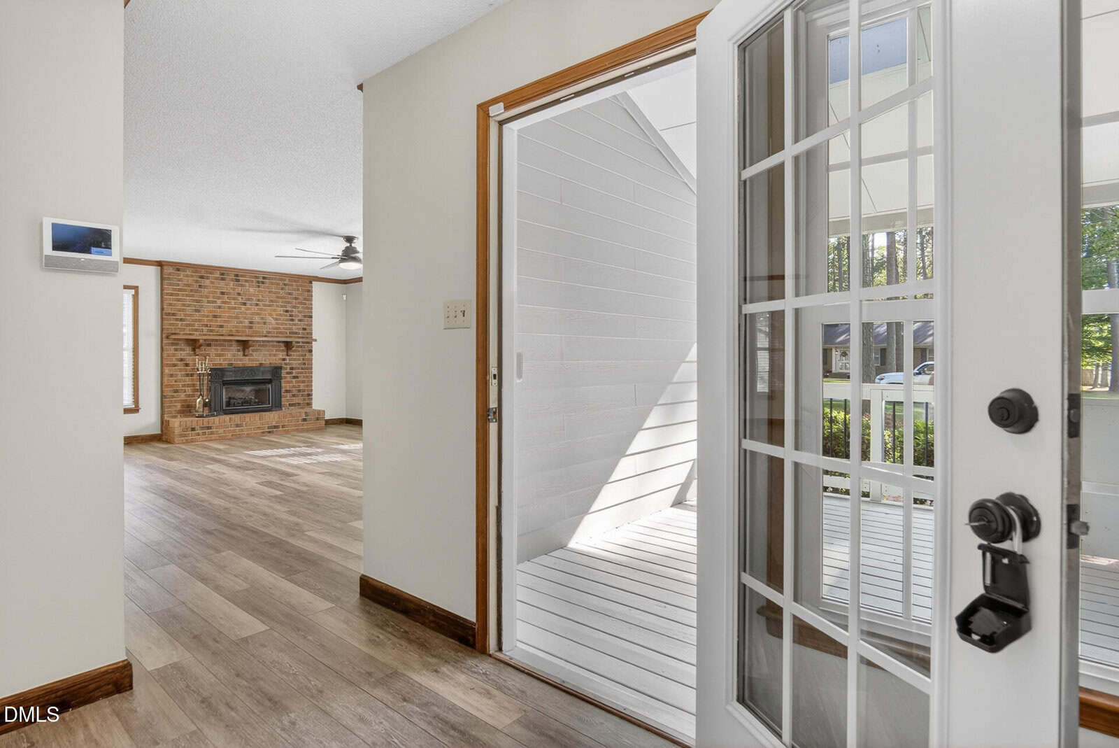 View from an open white door into a home entryway with wood-look floors, a brick fireplace in the living room, and a porch area visible through the glass.