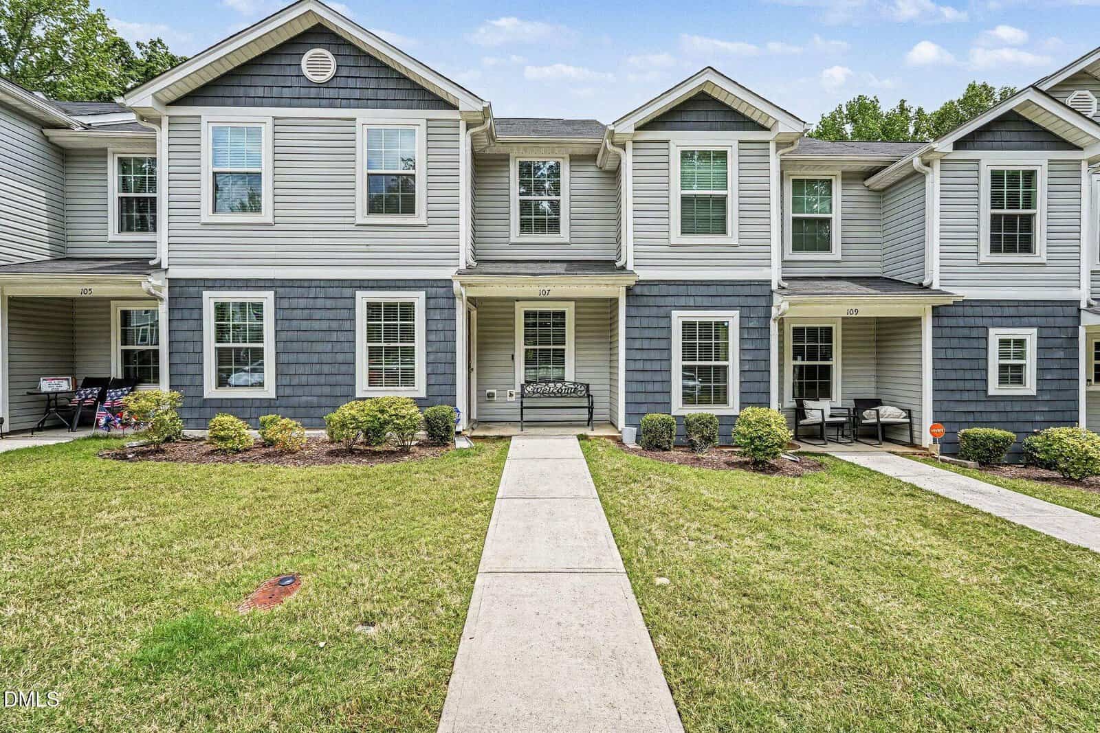 Located in Franklinton, 918 E Green Street Unit G107 is a two-story townhouse with gray siding, white trim, and a covered entryway. Trimmed bushes and a green lawn border the walkway to the front door, with neighboring units on both sides.