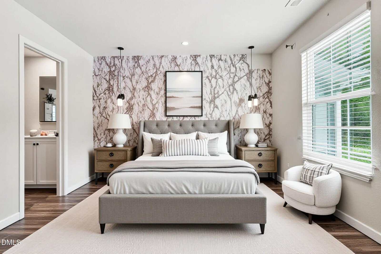 A modern bedroom features a gray upholstered bed with striped pillows, marble-patterned accent wall, two wooden nightstands with lamps, a framed art print, a small armchair, and a window with blinds letting in natural light.