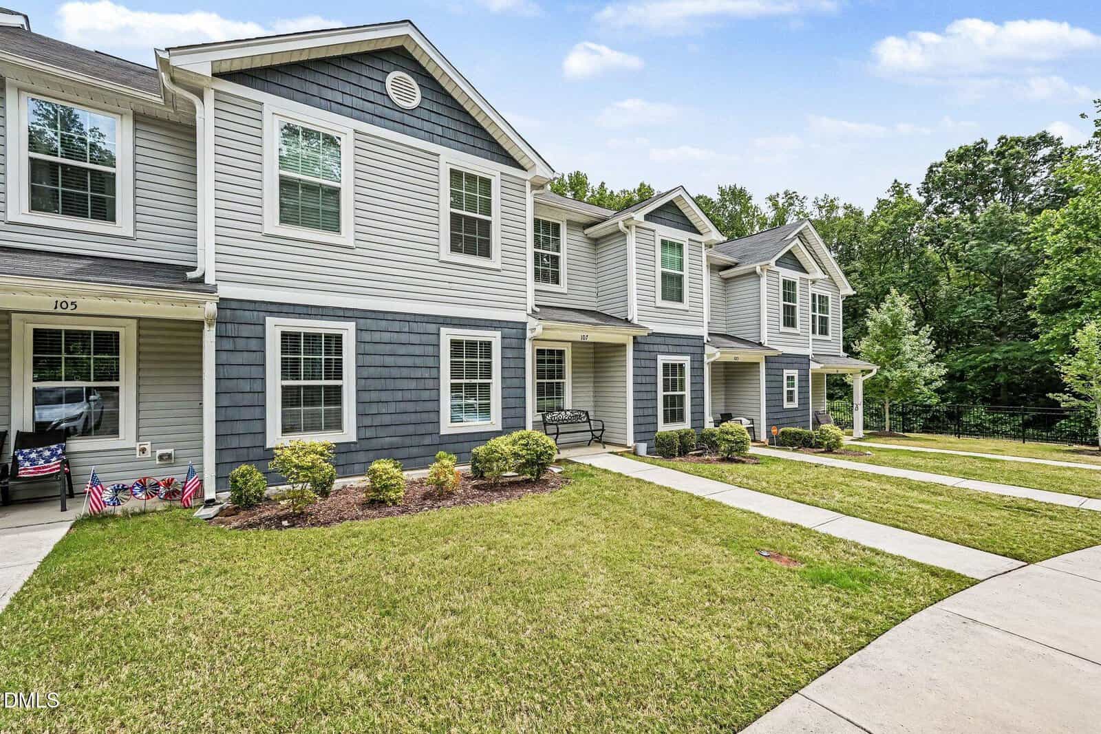 A row of modern two-story townhouses in Franklinton with gray siding, white trim, and small landscaped front yards lines 918 E Green Street Unit G107, set along a curved sidewalk with trees and greenery in the background.