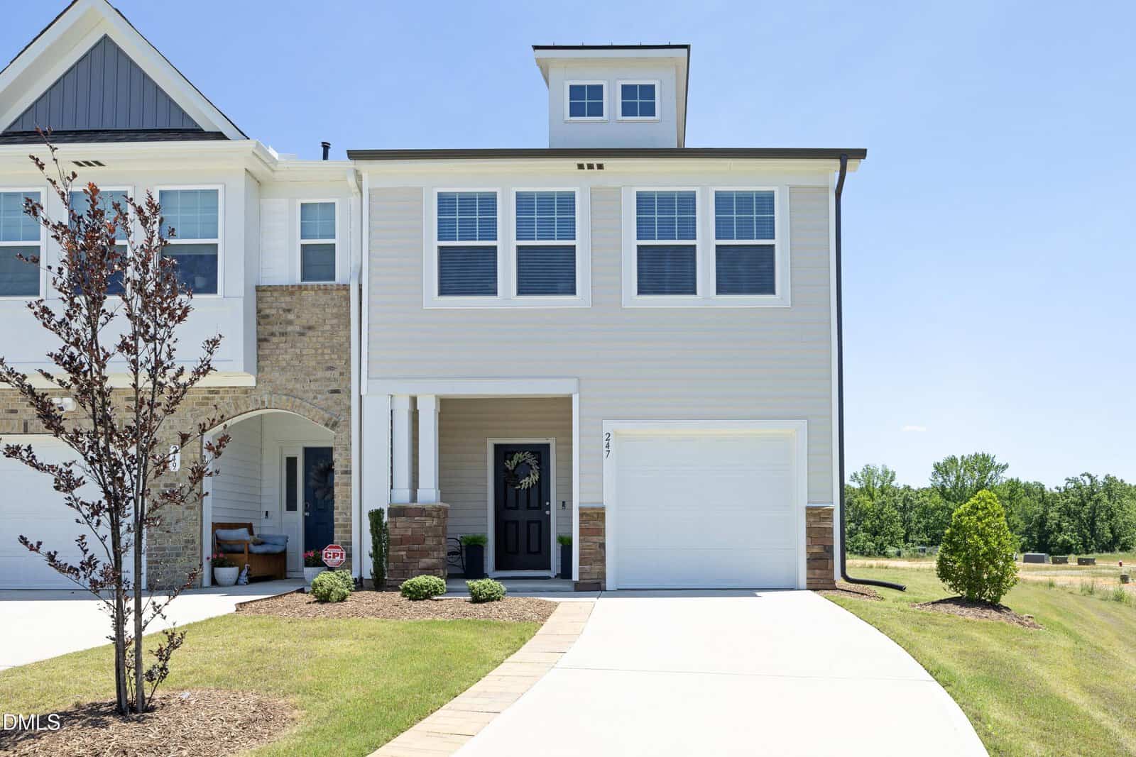 This modern two-story townhouse on 247 Blandford Street in Franklinton features light gray siding, white trim, and a single-car garage. A small tree and neat landscaping adorn the front yard beneath a clear blue sky.
