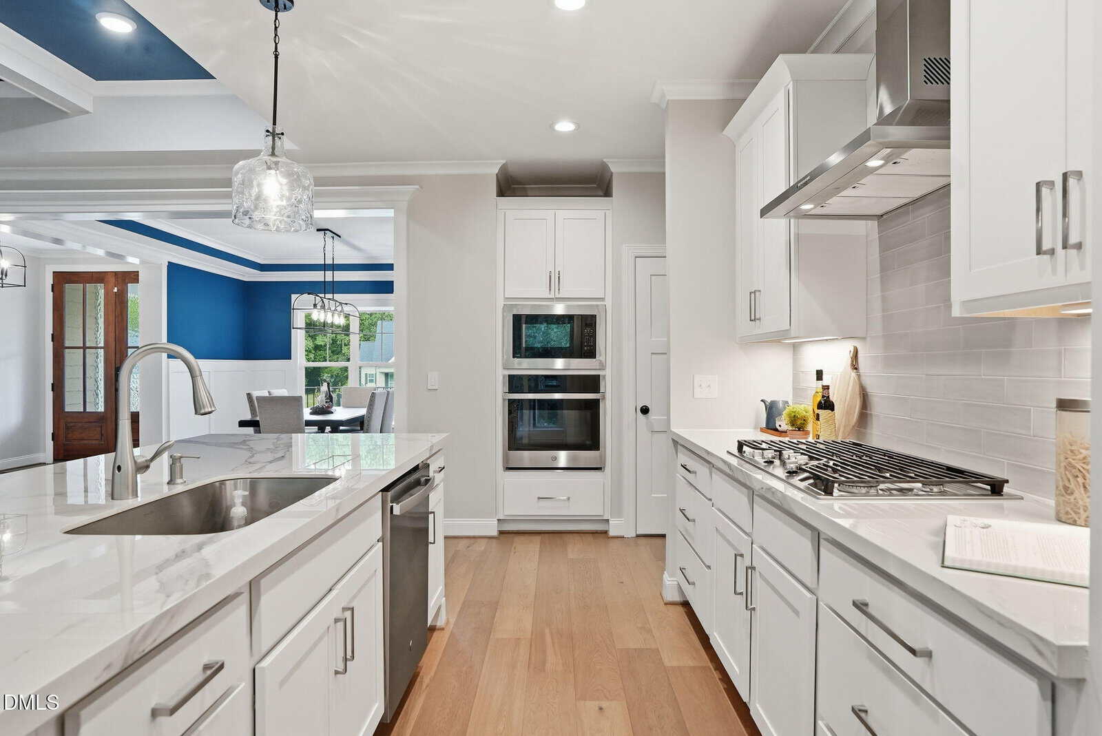 Modern kitchen with white cabinets, marble countertops, stainless steel appliances, and a center island with a sink; open floor plan leads to a living area with blue accent walls and large windows.