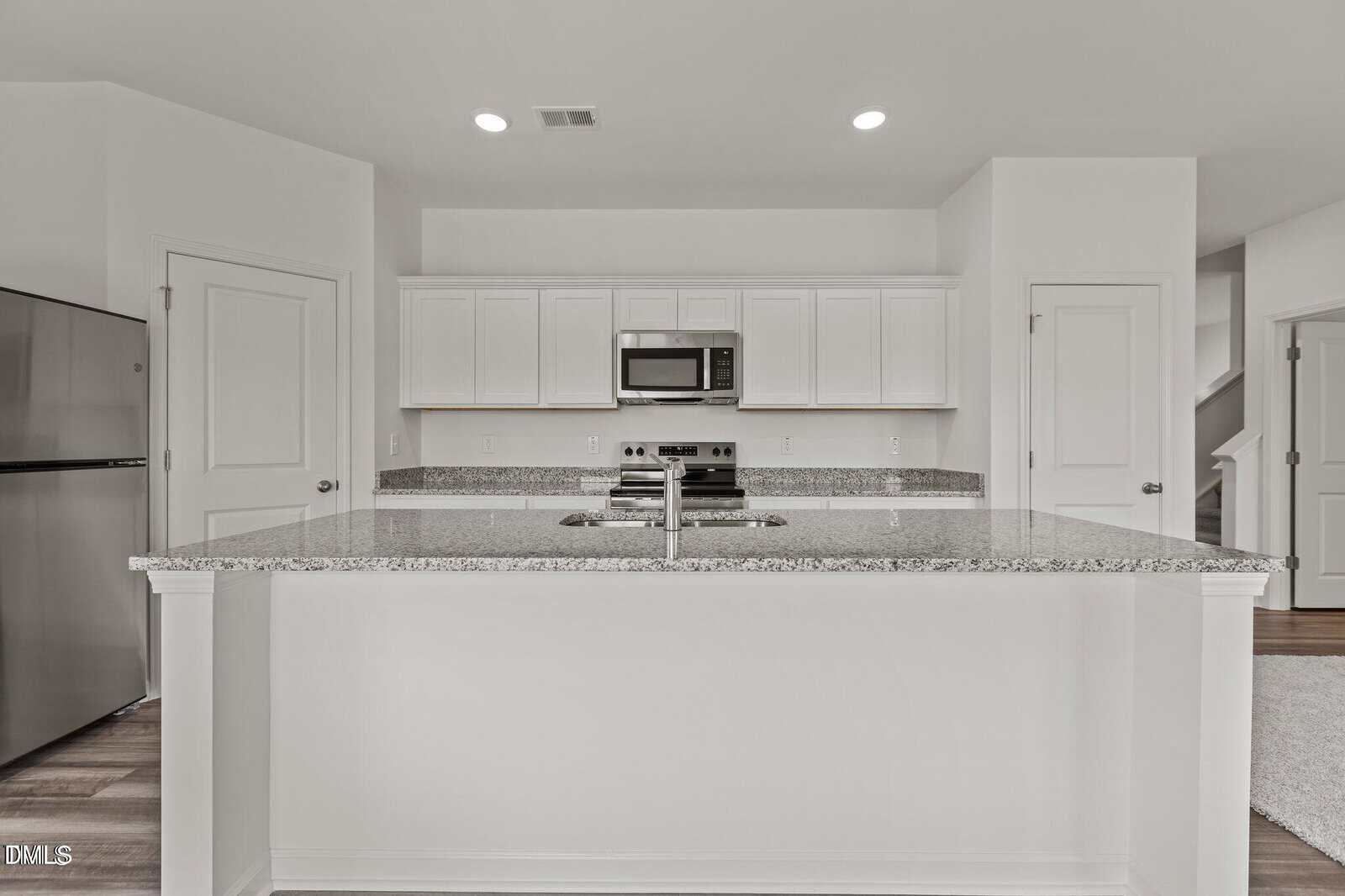 Modern kitchen with white cabinets, granite countertops, stainless steel appliances, built-in microwave, and a large island with a sink. The space is bright with recessed lighting and minimal decor.