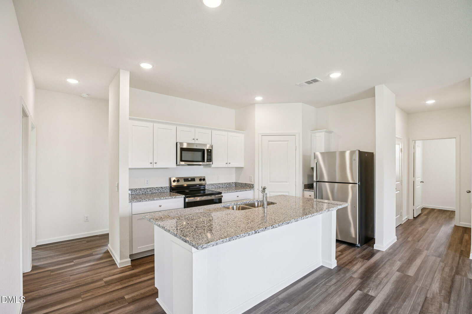 Modern kitchen with white cabinets, granite countertops, stainless steel appliances, and a central island with a sink. The space features wood-style flooring and recessed lighting, with doorways leading to other rooms.