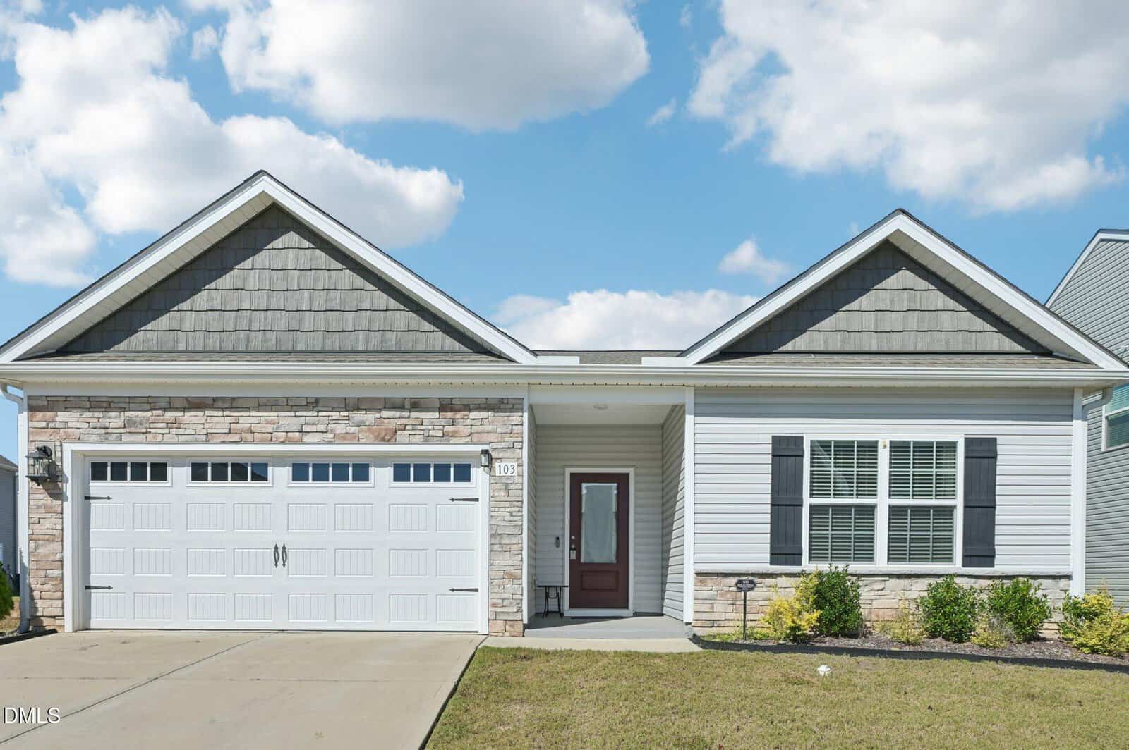 Charming single-story suburban house at 103 Blue Hydrangea Way, Youngsville, with two gabled roofs, stone and siding exterior, double garage doors, a red front door, small porch, manicured lawn, and a blue sky with scattered clouds.