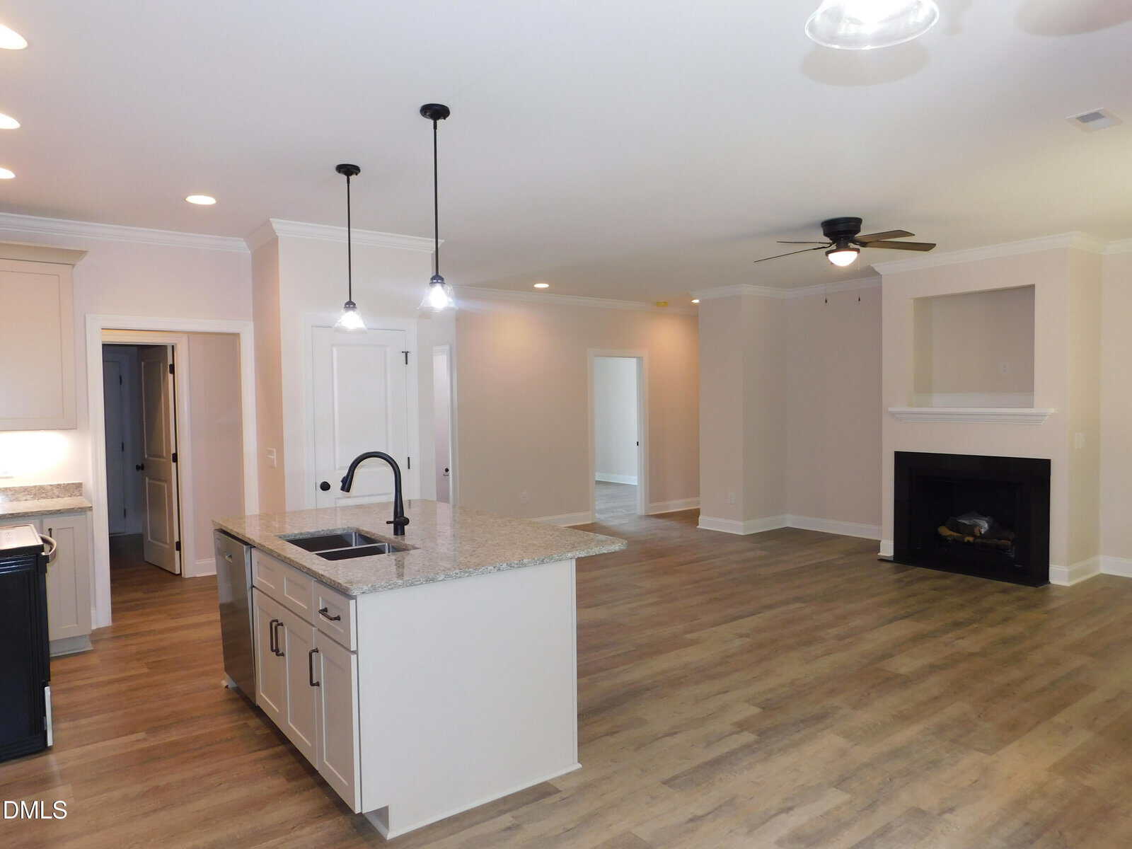 Modern open-concept kitchen and living room with light wood floors, white cabinets, a large island with a sink, ceiling fan, fireplace, and recessed lighting. Multiple doors lead to other rooms.