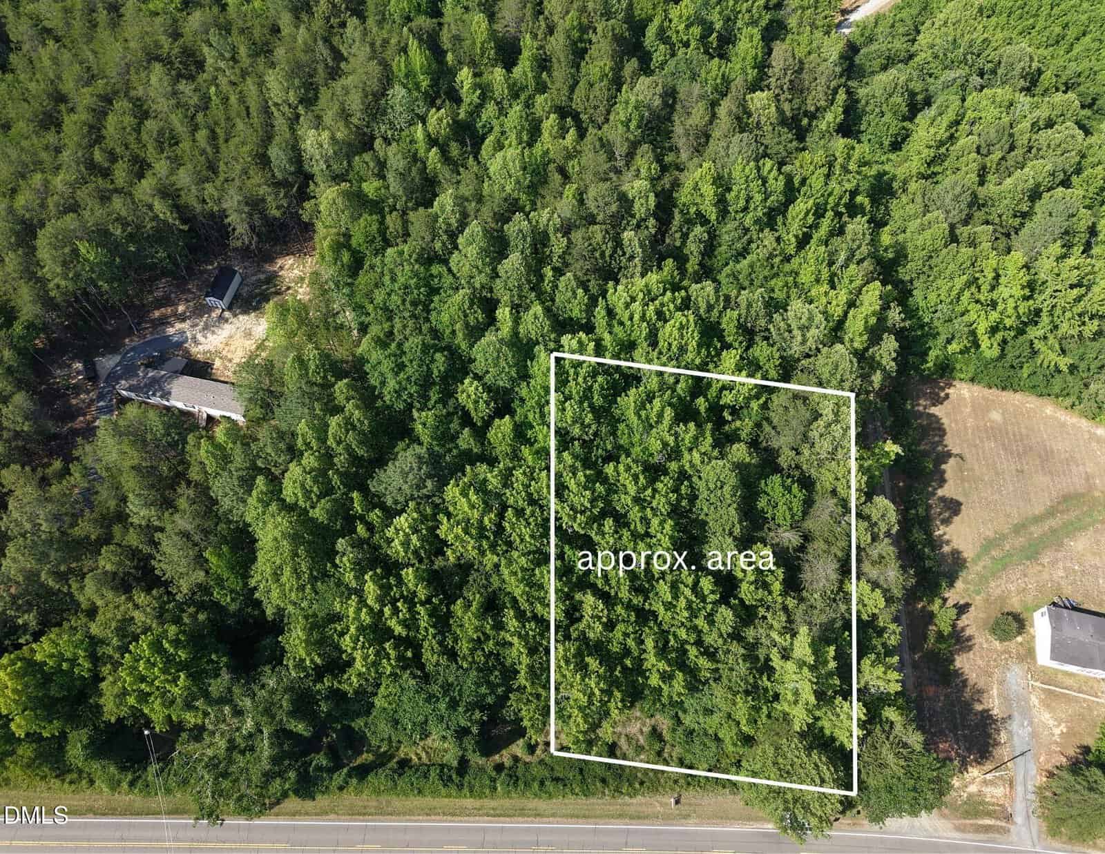 Aerial view of a wooded lot bordered by a road at the bottom. A white outlined rectangle marks an "approx. area" within the trees, near some cleared land and a house at the left edge.