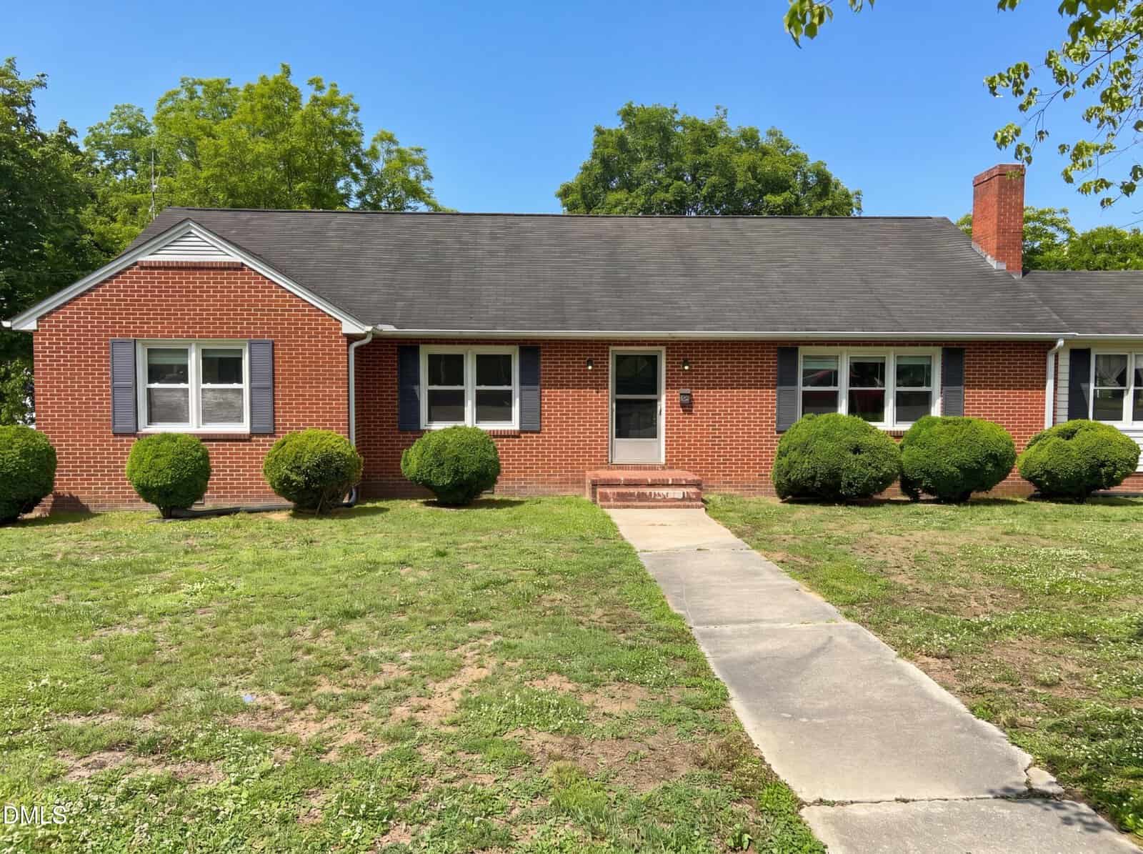 Charming single-story red brick house at 309 Broad Street, Oxford, with black shingle roof, white trim, two front windows with dark shutters, a right-side chimney, trimmed shrubs, and a concrete walkway to the entrance.