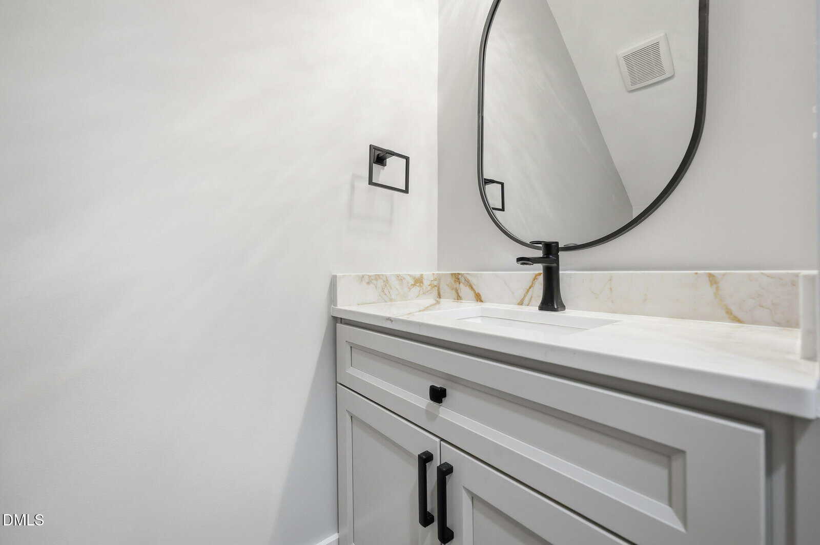 A modern bathroom with a white vanity, marble countertop, black faucet, oval mirror, and towel holder on a white wall.