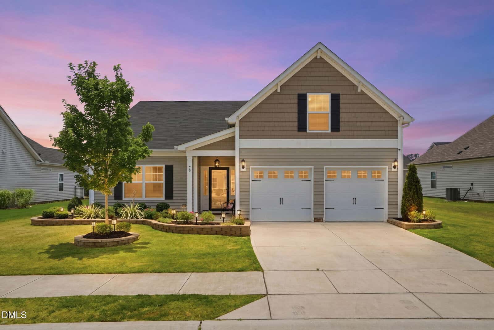 A single-story suburban house at 73 Sugarmaple Way, Youngsville, with beige siding, a covered entryway, two-car garage, and well-kept lawn, pictured at sunset under a pink and purple sky. Shrubs and a tree decorate the front yard.