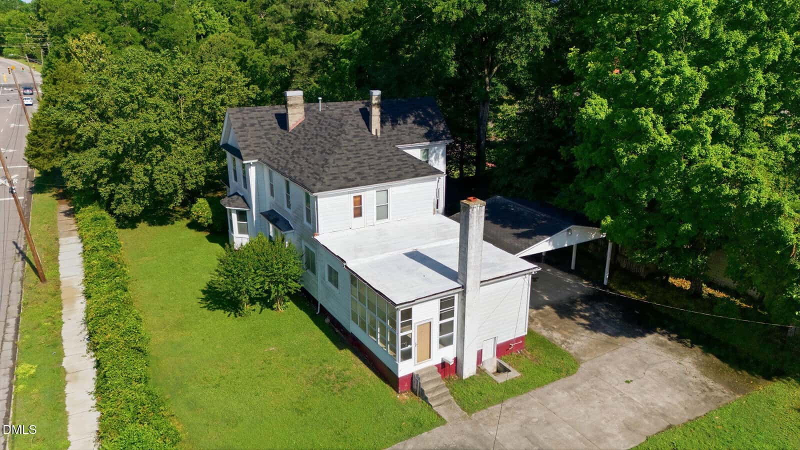 Aerial view of a two-story white house with a black roof, sunroom, and carport at 845 S William Street in Henderson, surrounded by green trees and grass, next to a sidewalk and road.