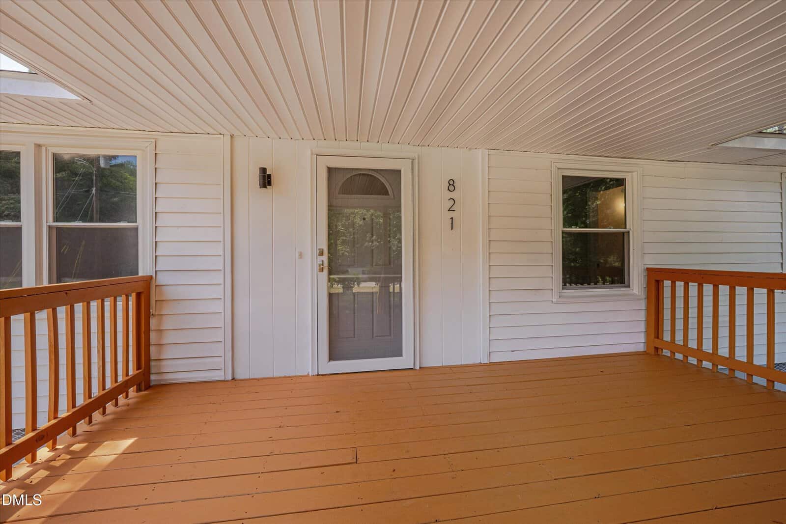 A covered porch with light brown wooden flooring and railing, white siding, two windows, and a glass-paneled door with the house number 821 displayed vertically next to it.