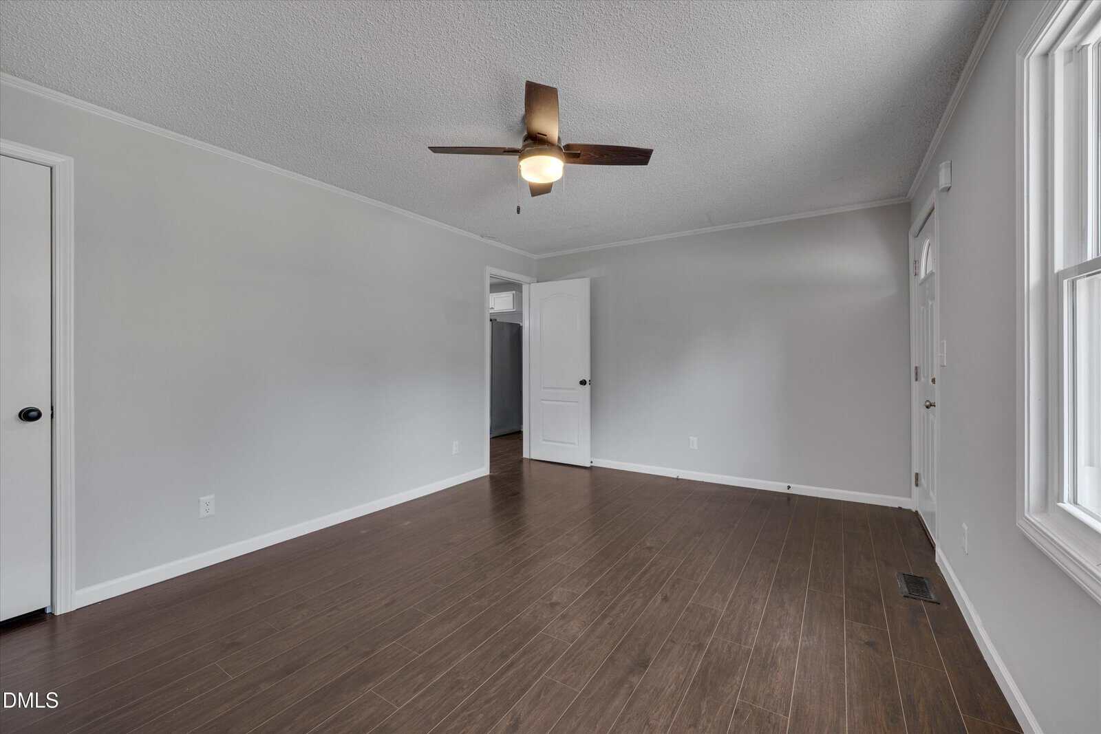 Empty room with dark wood floors, light gray walls, a ceiling fan with light, white trim, and two doors. Sunlight enters from a window on the right side of the image.