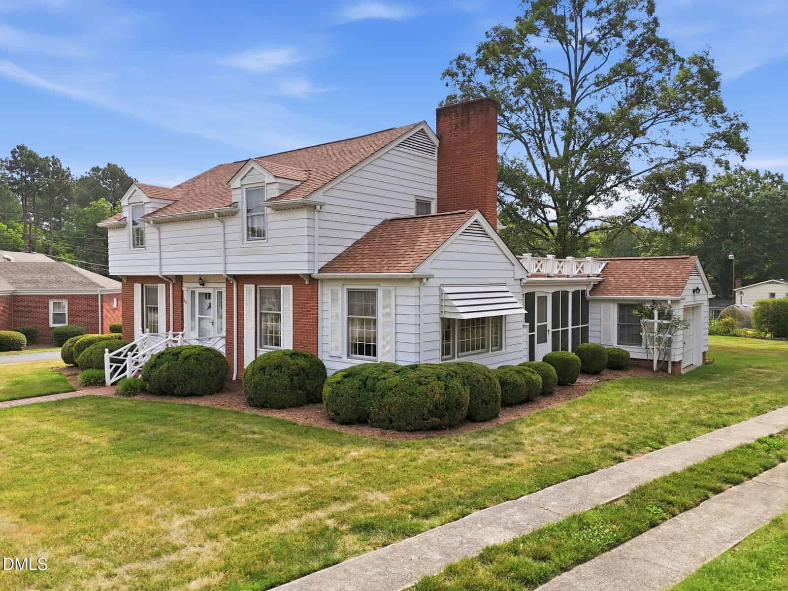 Charming two-story white house at 203 Hillcrest Drive, Oxford, with red shingle roof, prominent brick chimney, and large bushes. Features a sunroom with white trim on a grassy corner lot with sidewalks.