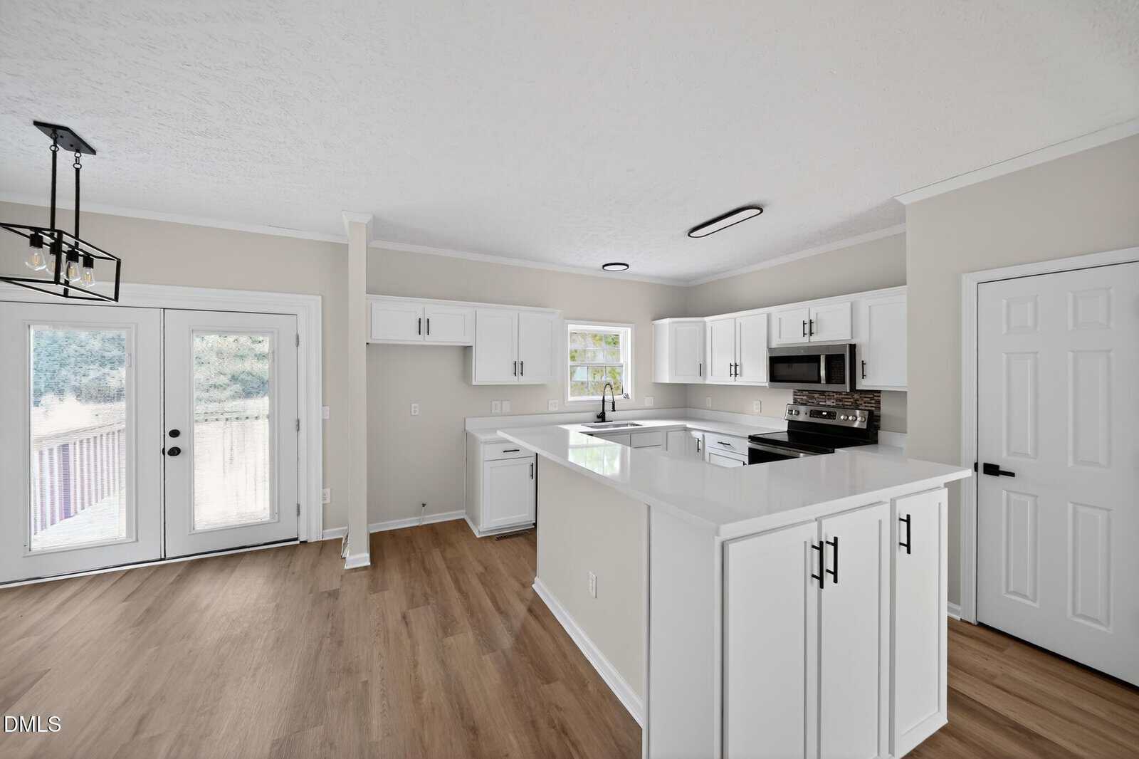 Bright modern kitchen with white cabinets, stainless steel appliances, light wood flooring, a center peninsula, and double glass doors leading outside. A window above the sink lets in natural light.