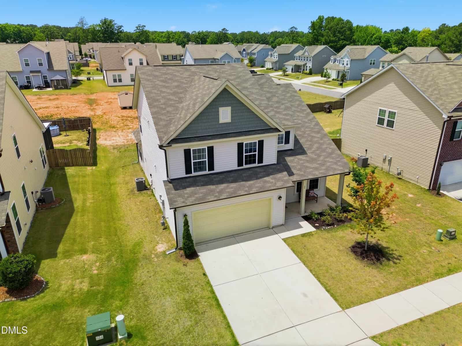 A two-story suburban house at 20 Saintsing Trail, Franklinton, with light-colored siding, a covered front porch, and an attached garage sits amid a neat lawn. Neighboring houses and a partially undeveloped lot are visible in the background.