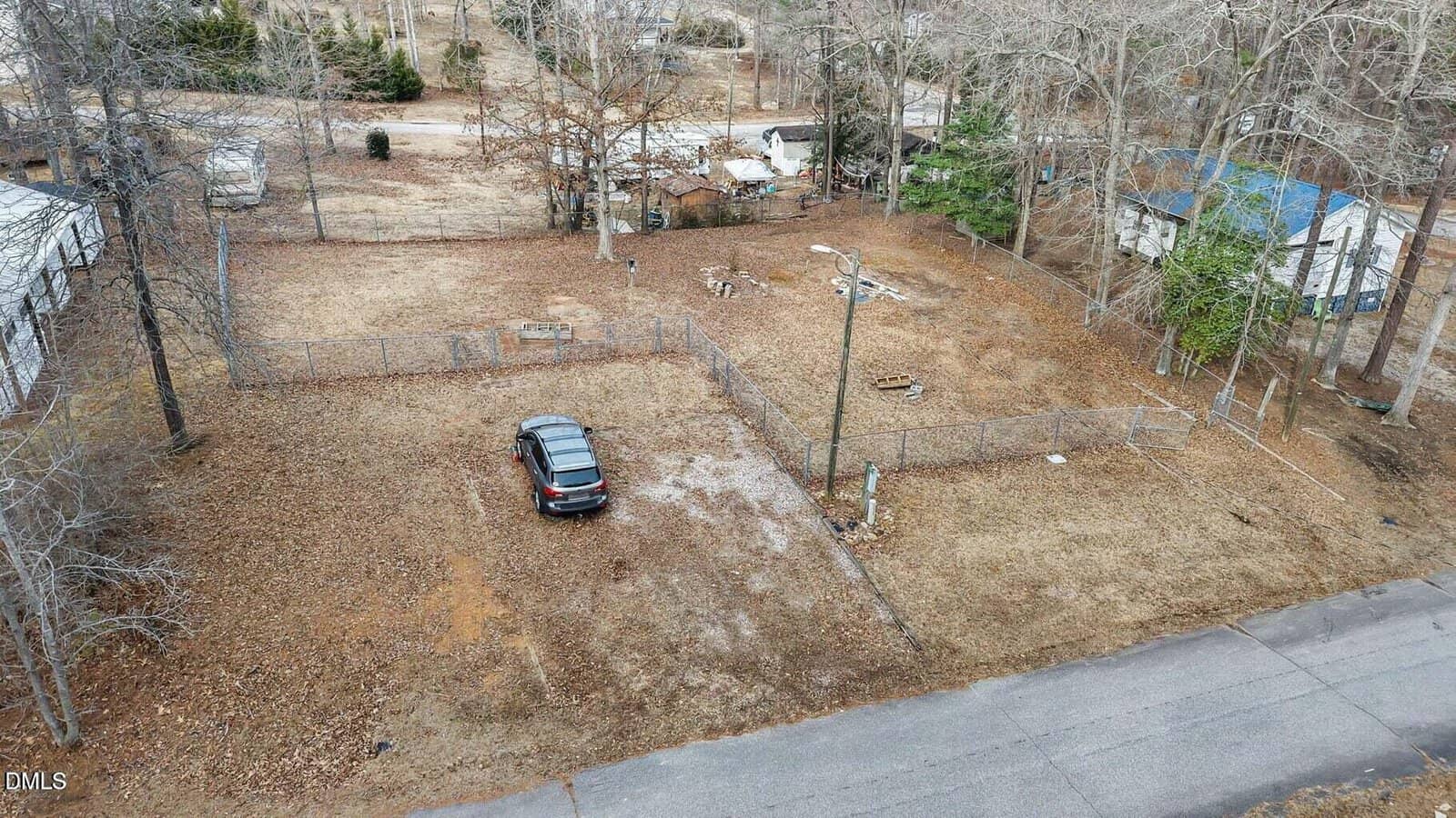 Aerial view of a fenced, mostly bare yard at 137 Tonto Drive, Louisburg, with a single parked car near the center, surrounded by trees and neighboring houses on a residential street.