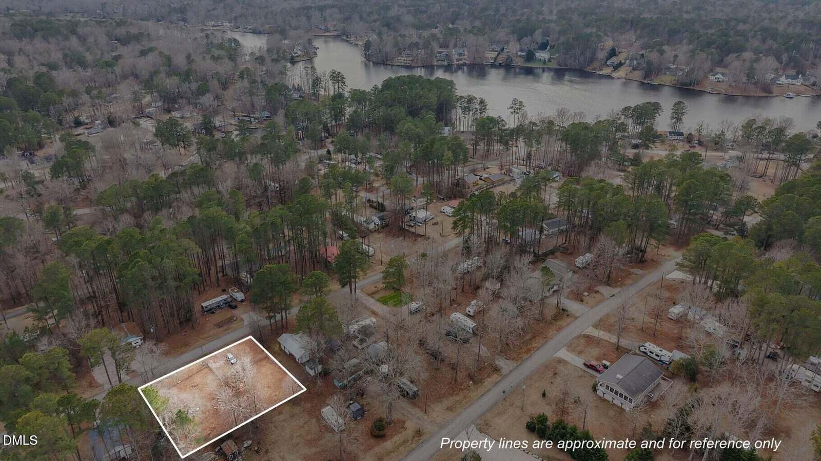 A wooded residential neighborhood with a highlighted empty lot in the foreground, surrounded by trees and houses, near a lake in the background. Text notes property lines are approximate and for reference only.