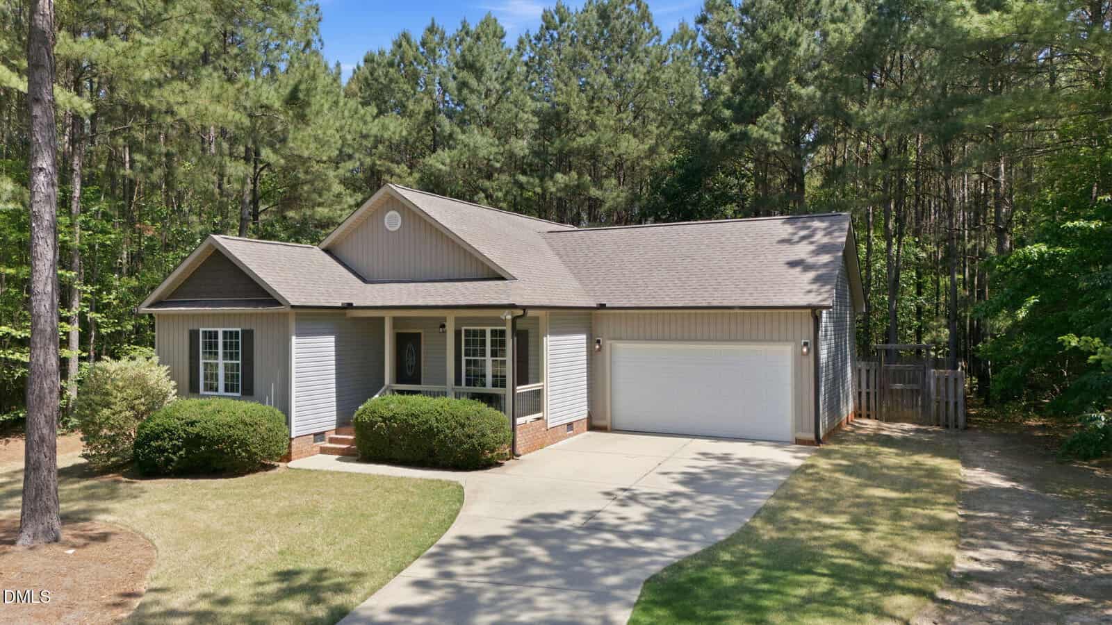 Charming single-story house at 1205 Bayview Court, Franklinton, with gray siding, a front porch, white trim, and a two-car garage. Surrounded by pine trees and a lush lawn, a curved driveway leads to the inviting garage.