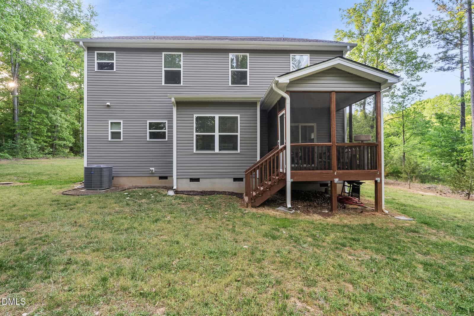 Two-story gray house with white trim, screened-in porch, wooden steps, and a grassy backyard bordered by trees. An air conditioning unit sits on the left side near the house.