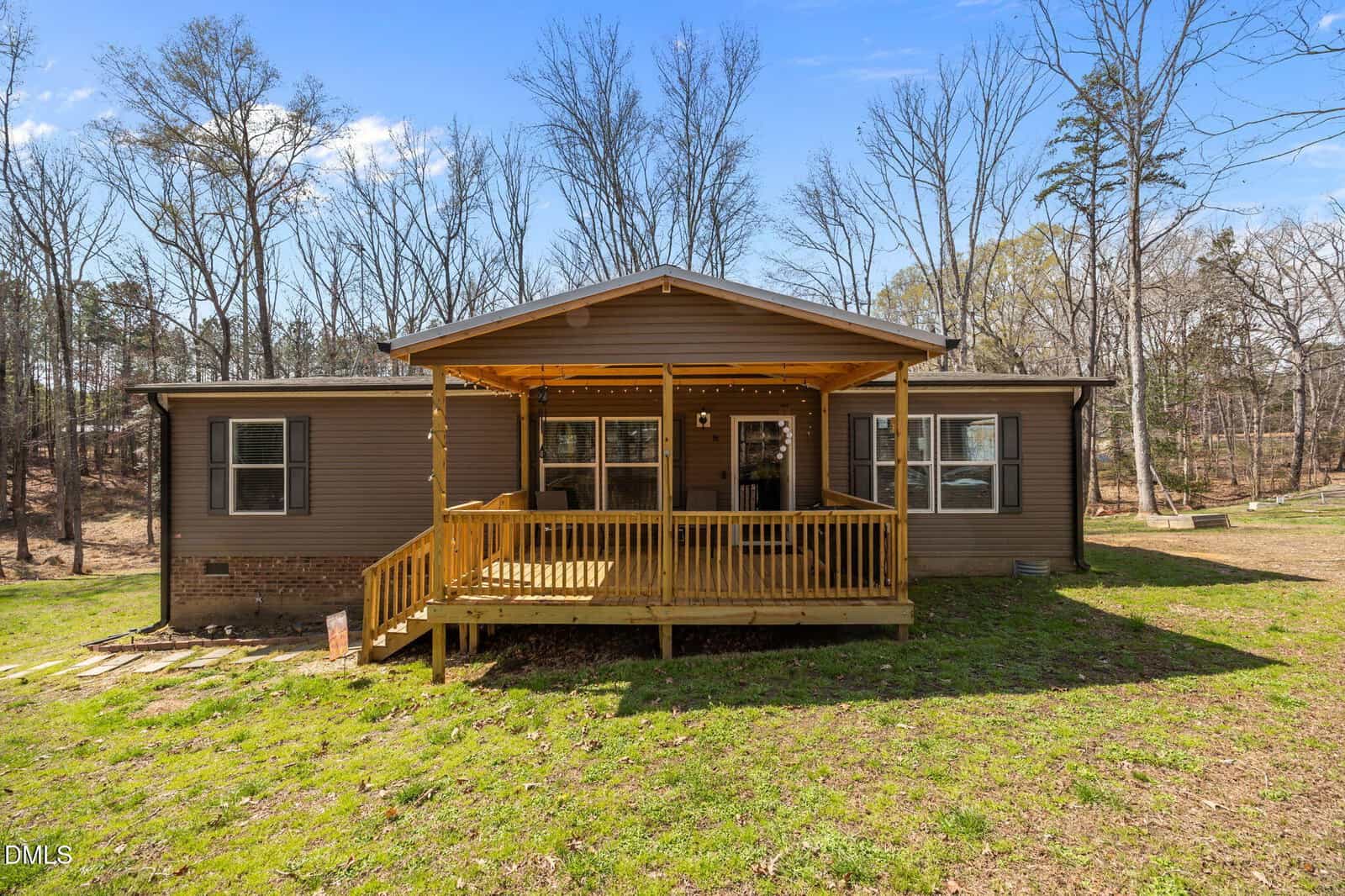 A brown single-story house with a covered wooden front porch, surrounded by grass and trees with no leaves, under a clear blue sky.