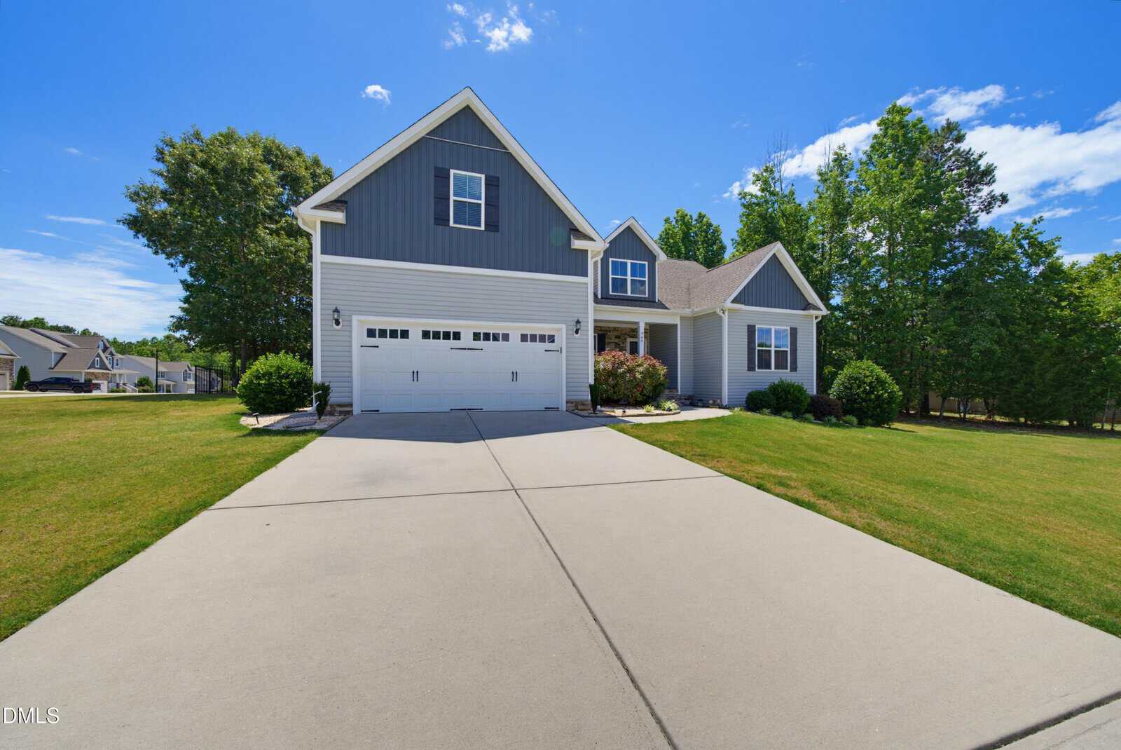 A modern gray house with white trim at 60 Anna Marie Way, Youngsville, features a front lawn and double garage, set on a sunny day with clear blue sky and surrounded by trees and greenery.