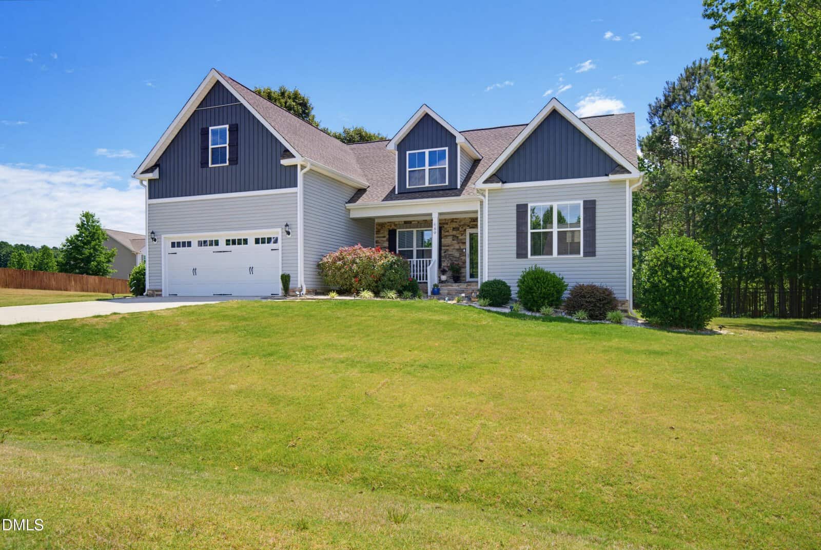 A modern gray house with white trim, a double garage, and a well-maintained front yard with green grass, small shrubs, and trees in the background under a clear blue sky.