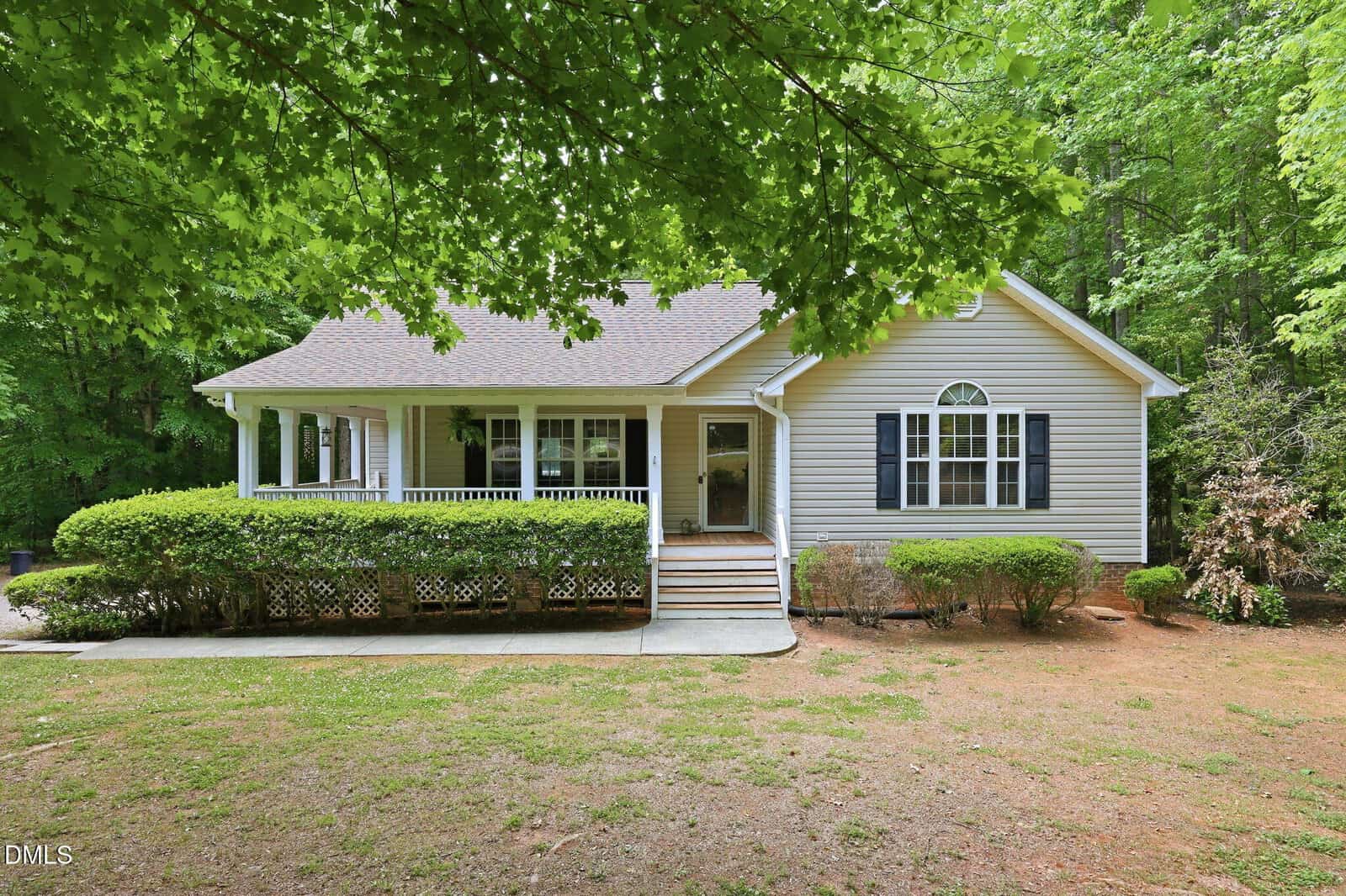 Charming single-story house at 220 Hardwood Drive, Franklinton, with light gray siding, black shutters, and a covered front porch. The yard features sparse grass, bushes, and is surrounded by mature trees.