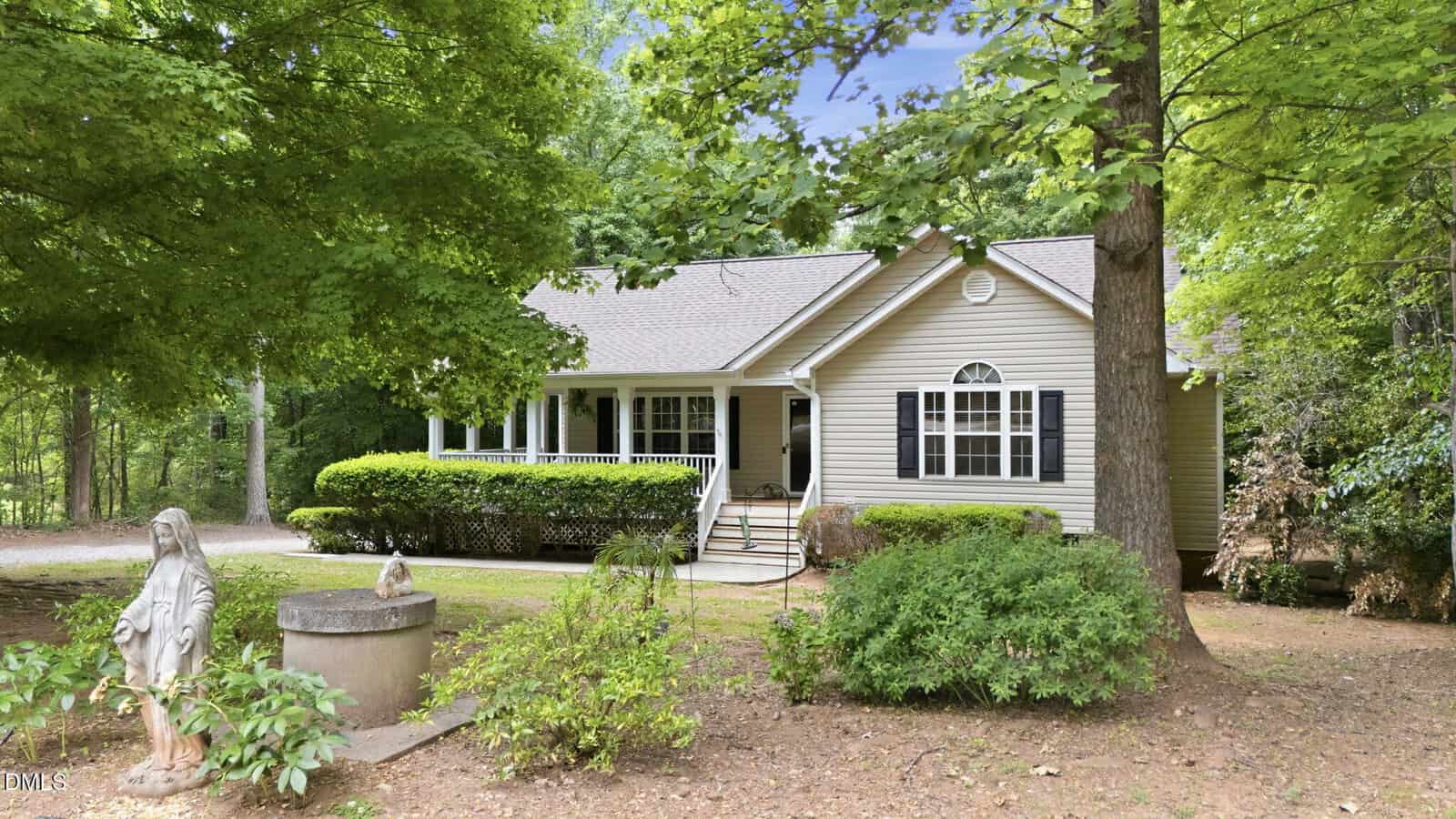 Nestled among tall green trees in Franklinton, 220 Hardwood Drive is a beige house with white trim and a front porch. A gravel path leads to the entrance, with a statue and well feature highlighting the landscaped front yard.