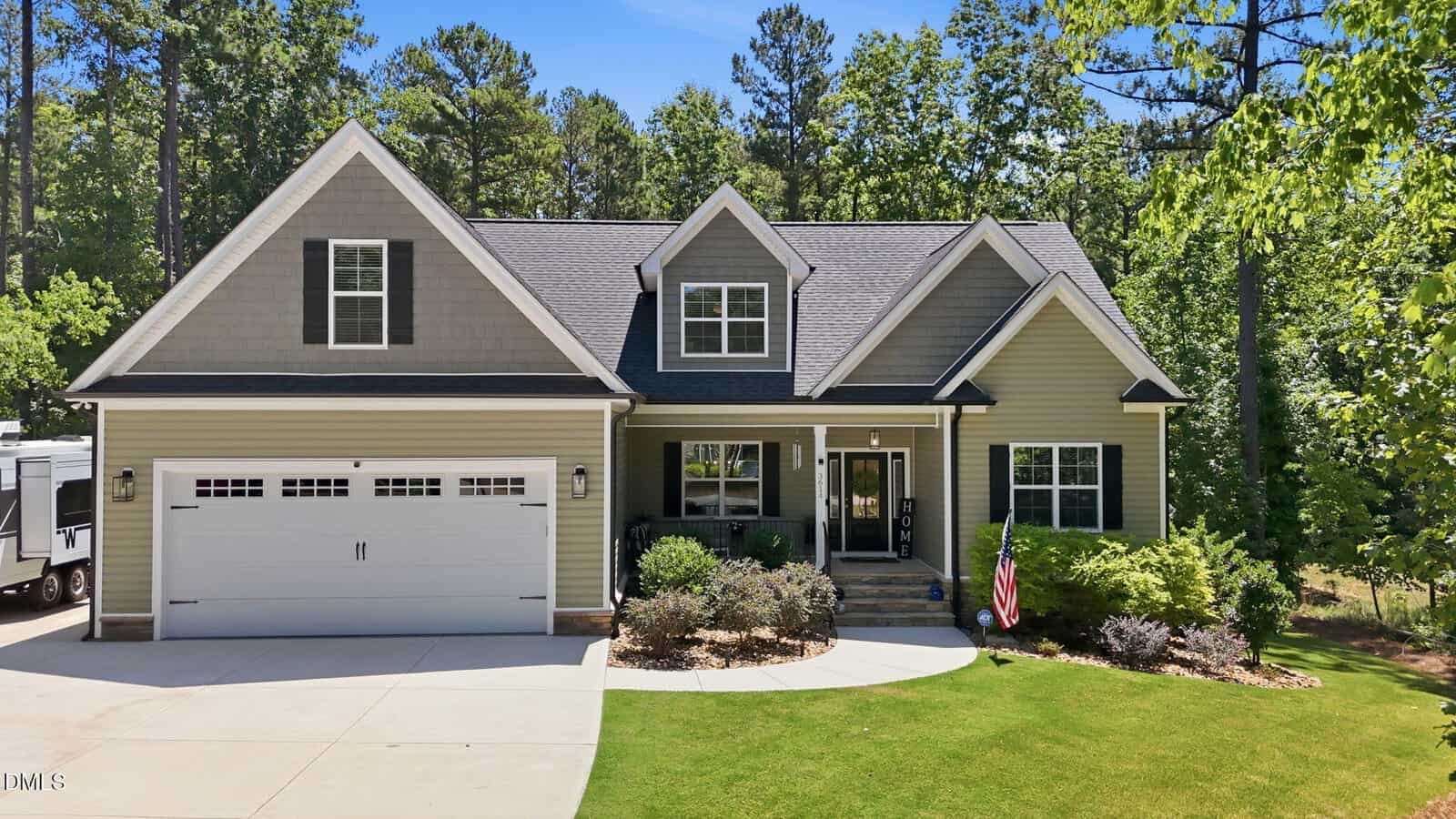 A two-story suburban house with gray siding at 3614 River Watch Lane, Franklinton, features a double garage, front porch, manicured lawn, landscaped shrubs, and tall trees on a sunny day. An American flag is displayed near the entrance.