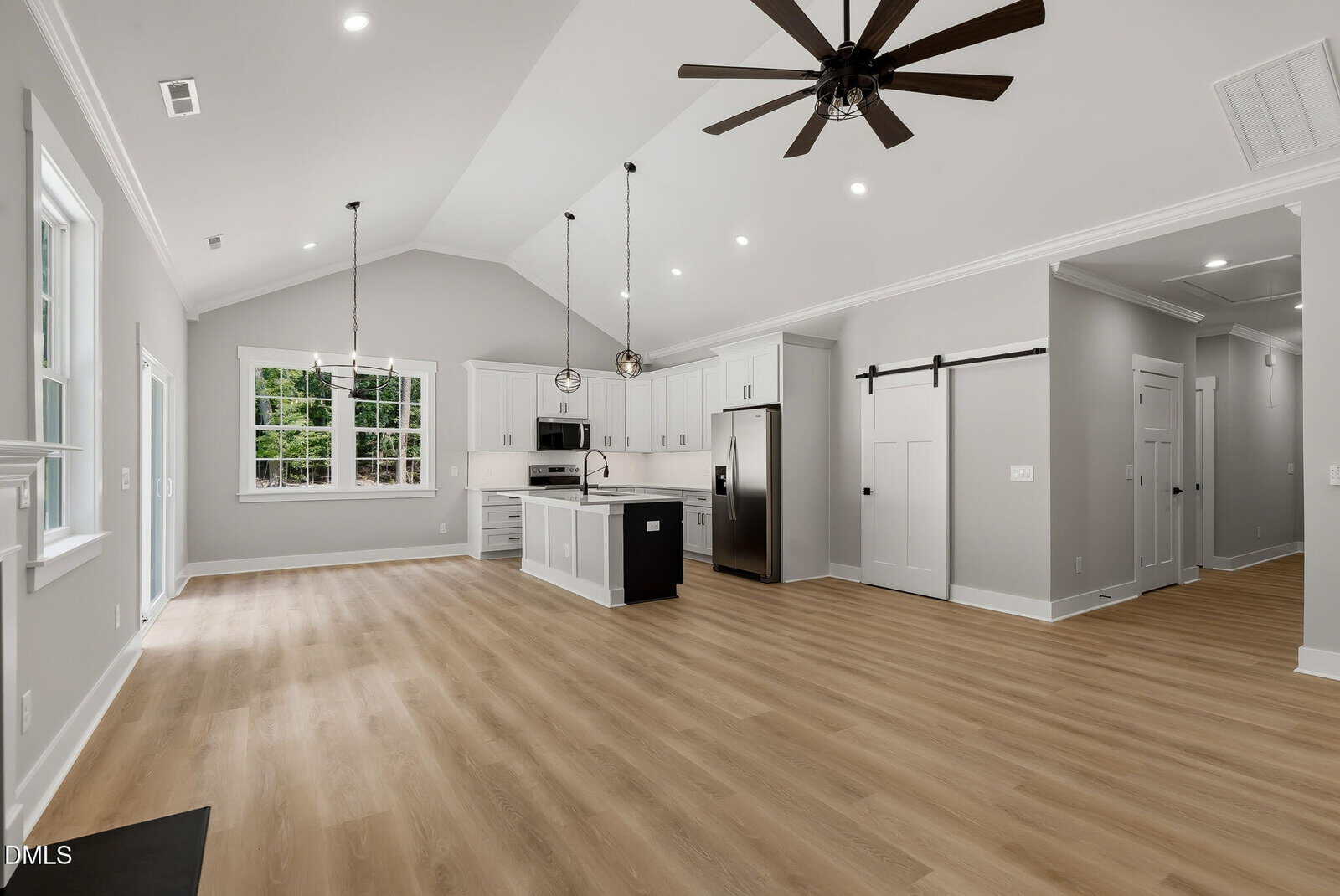 Modern open-concept kitchen and living space with light wood floors, white cabinets, stainless steel appliances, pendant lights, and a ceiling fan. Large window lets in natural light.