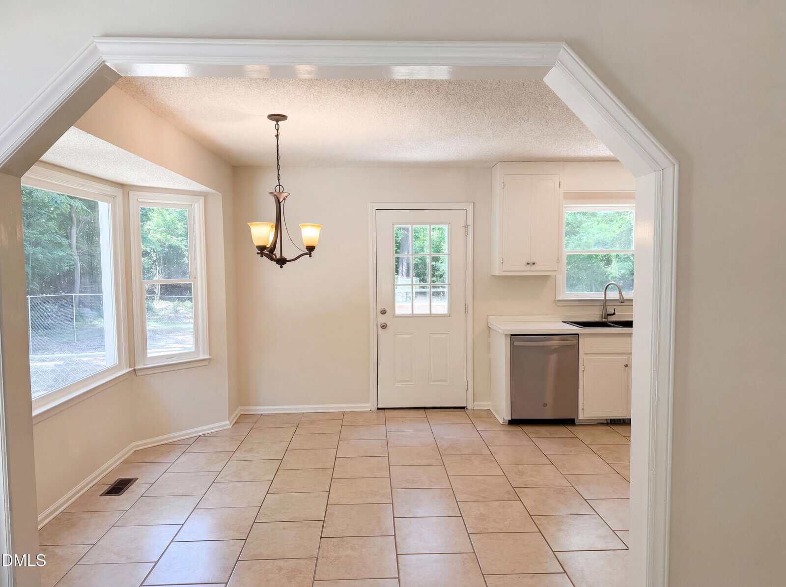 Bright kitchen and dining area with tile floors, white cabinets, stainless steel appliances, a window over the sink, bay windows, a chandelier, and a door leading outside.