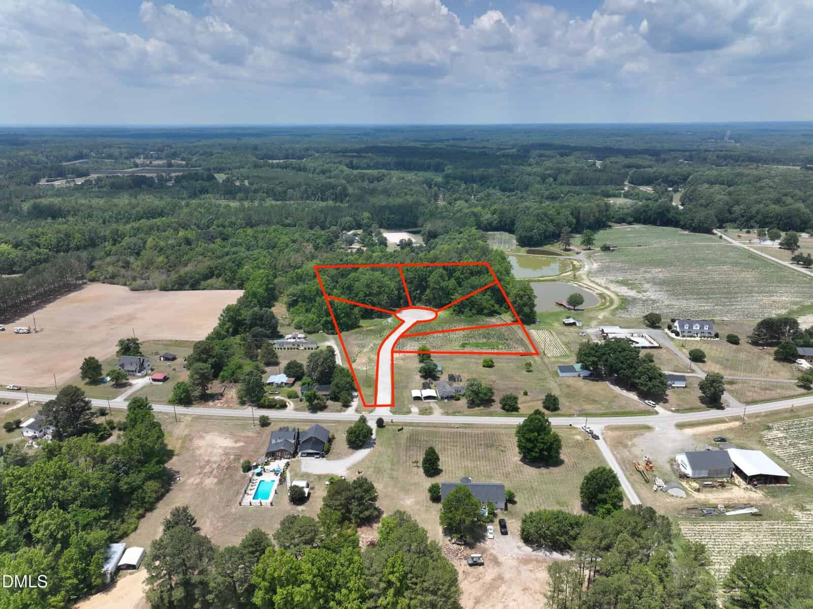 Aerial view of a rural Louisburg landscape with trees, fields, and houses; a section of land on Tbd Wood Road is outlined in red, divided into lots along a curved driveway. Blue sky with scattered clouds overhead.