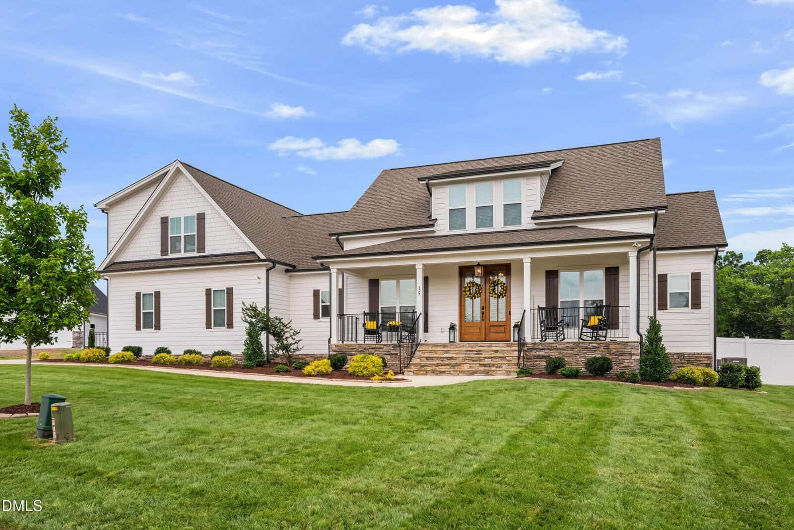 A large, modern farmhouse-style home at 15 Old Garden Lane in Youngsville, with white siding, a dark roof, and stone steps leading to a covered front porch. The yard is well-manicured with green grass, shrubs, and a small tree in front.