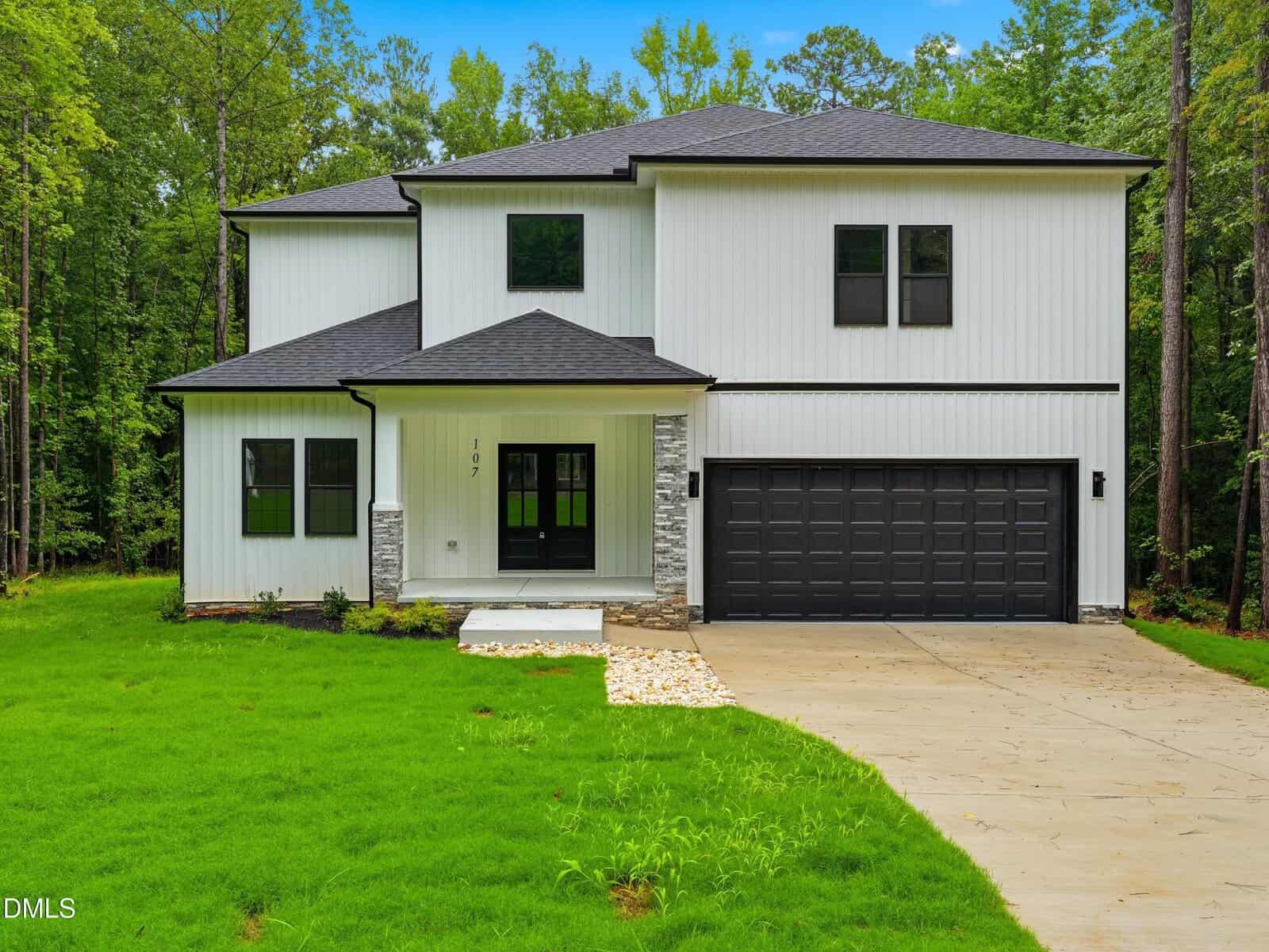 Modern two-story white house with black trim, a black double garage, covered front porch, stone accents, and a concrete driveway, surrounded by green grass and trees—perfectly situated at 107 Acoma Drive in the charming town of Louisburg.