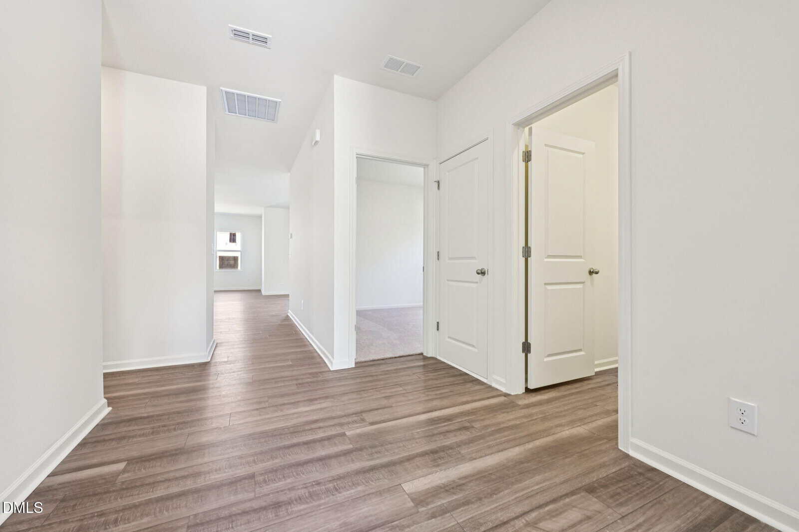 A bright hallway in a modern home with light wood floors, white walls, and several white doors leading to different rooms. Natural light enters from the far end of the hall.
