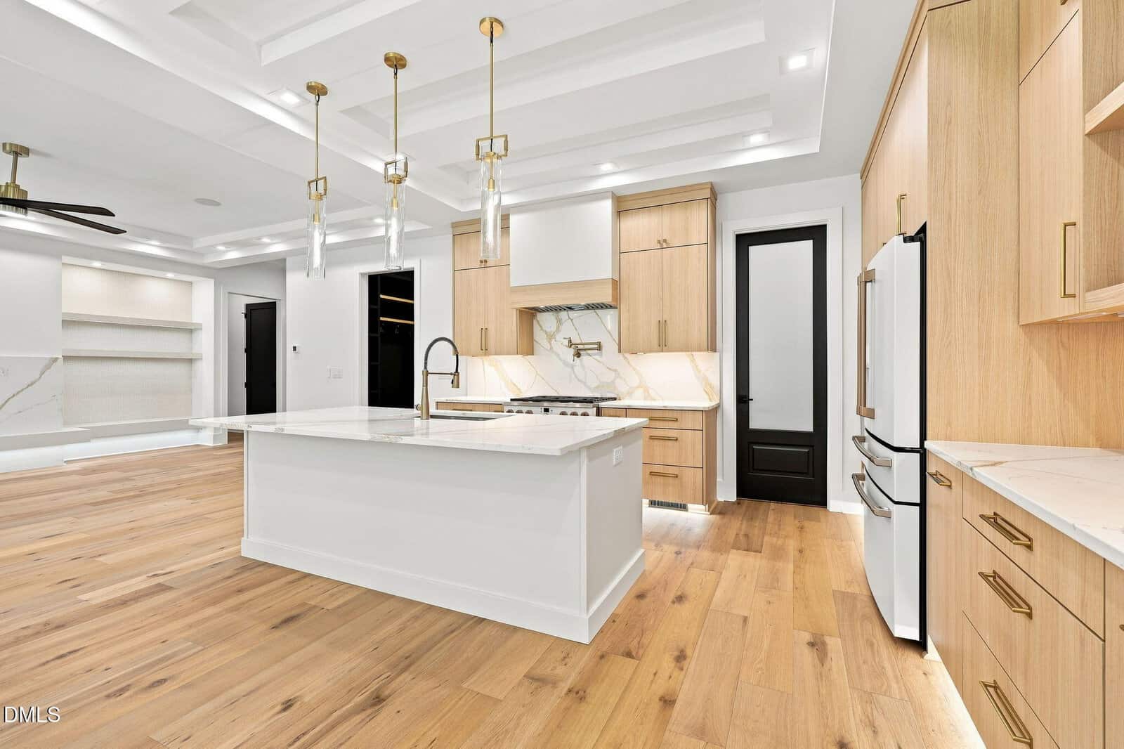 Modern kitchen with white island, gold accents, wood floors and cabinets, white marble backsplash, pendant lights, built-in appliances, and recessed ceiling lighting; open concept layout with bright and clean design.