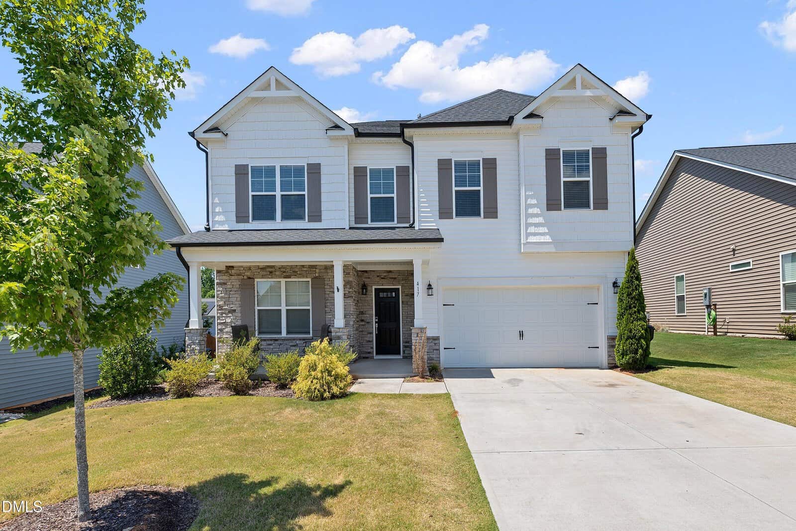 Two-story suburban house in Youngsville with white siding, gray shutters, a covered front porch with stone columns, and a double garage. Located at 417 Porterfield Drive, it features a small tree, shrubs, and a concrete driveway under a blue sky.