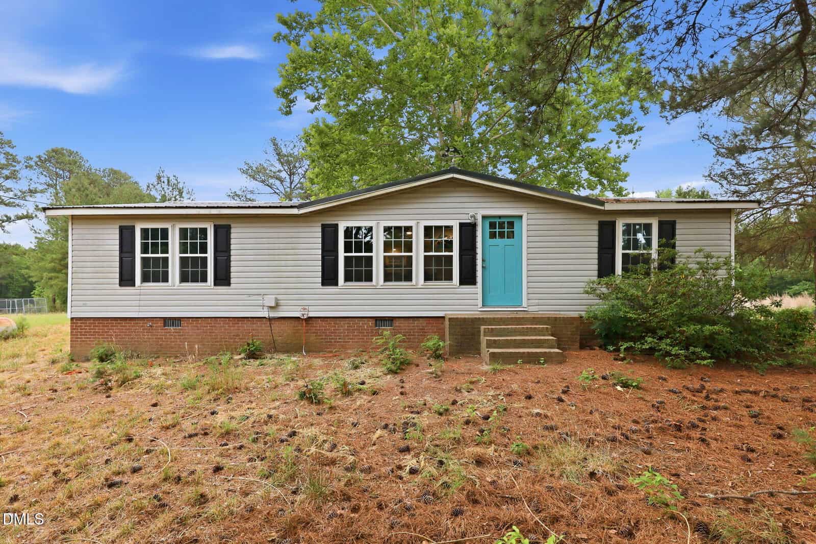 Charming single-story, light gray house with black shutters and a bright turquoise door at 3516 E Thollie Green Road, Stem, surrounded by pine trees and pinecones.